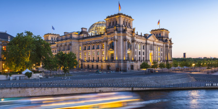 Motion blurred cruise boat passes in front of the mighty Reichstag parliament (1894) illuminated at night and reflected in th